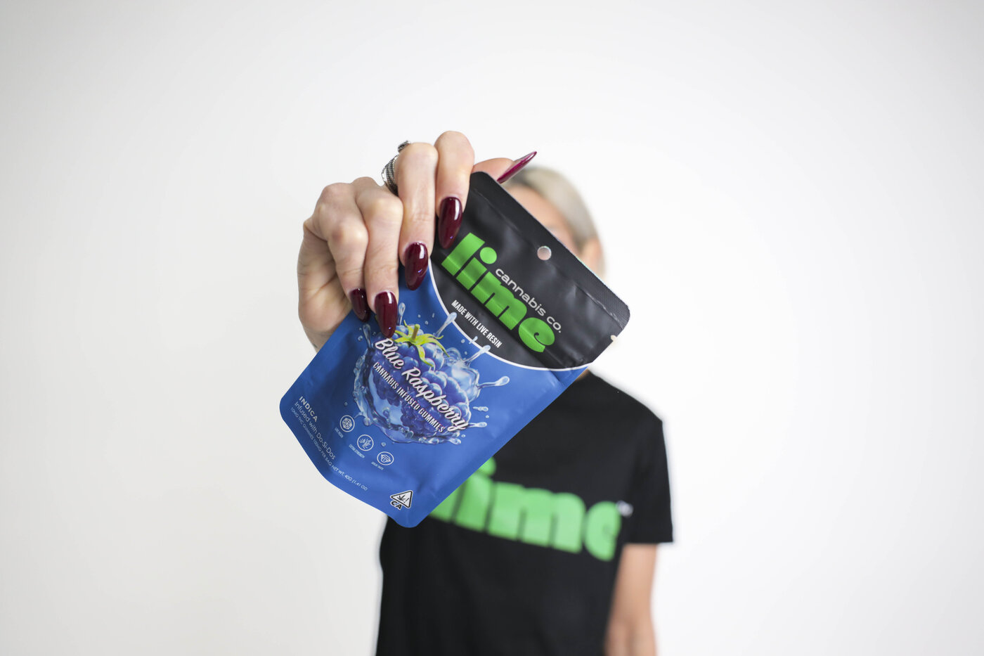 Lime Cannabis Co. Blue Raspberry gummies bag held by a customer wearing a Lime tee